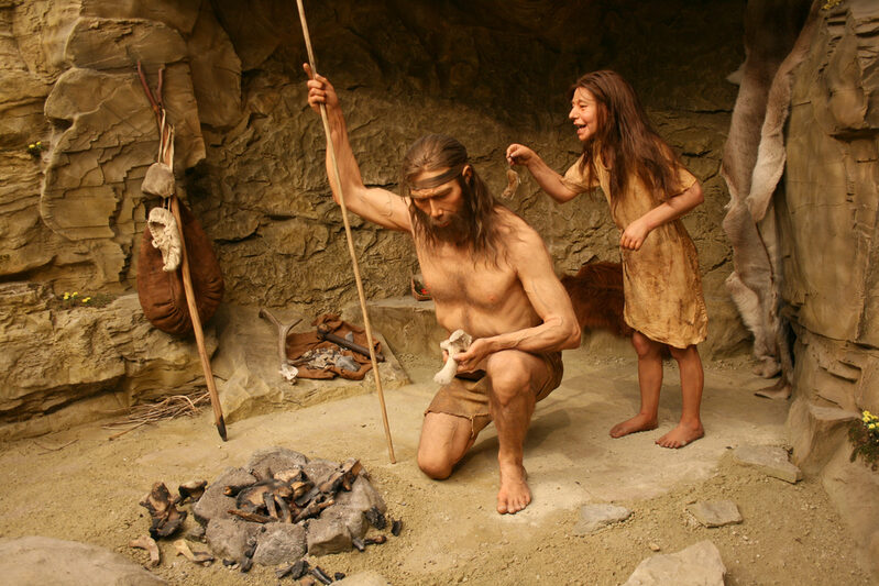 Steinzeitfamilie vor ihrer Höhle. Im Vordergrund eine Feuerstelle