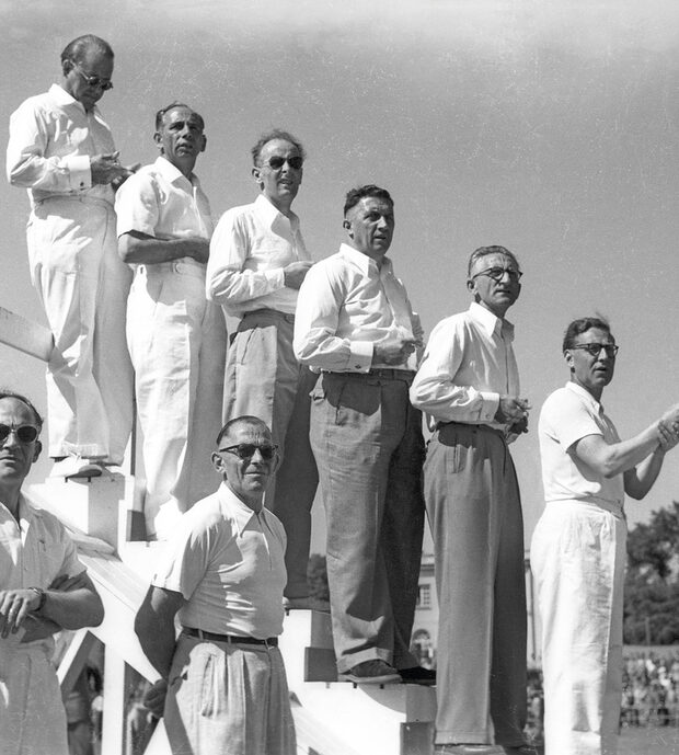 Zu sehen ist das Plakat zur Ausstellung mit einer Schwarzweißfotografie aus den 1950er Jahren, darauf zu sehen ist eine Gruppe von Männern